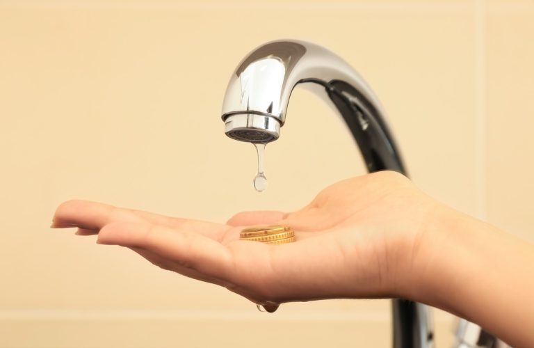 A close-up of a woman holding coins under a dripping metal faucet, illustrating how a high water bill during summer impacts household budgets.