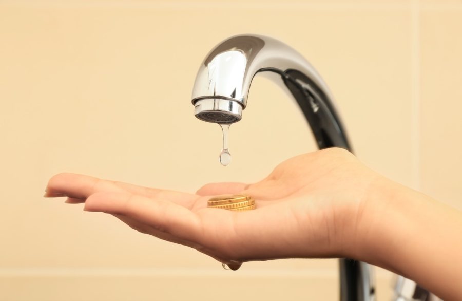 A close-up of a woman holding coins under a dripping metal faucet, illustrating how a high water bill during summer impacts household budgets.