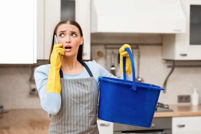 Homeowner with a bucket and apron trying to catch water from a pipe leak